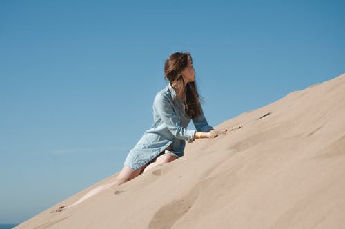 蓝色长袖衬衫坐在棕色的沙子上的女人 · 免费素材图片