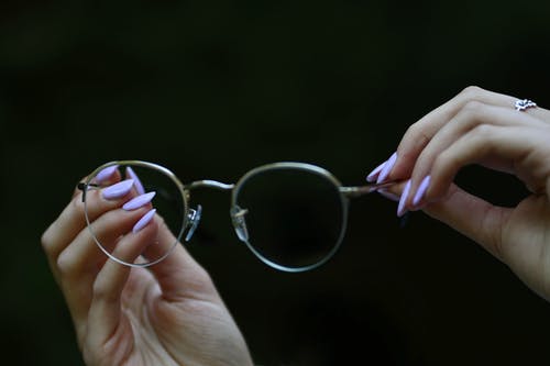 在黑色背景下手持眼镜的人的手的照片 · 免费素材图片