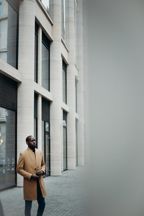 在建筑物外摆姿势的棕色大衣的男人的照片 · 免费素材图片