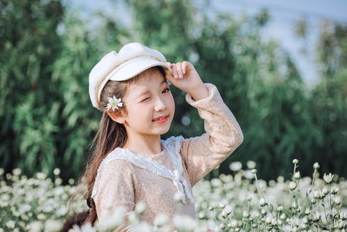 站在花旁边的女孩戴帽的选择性聚焦摄影 · 免费素材图片