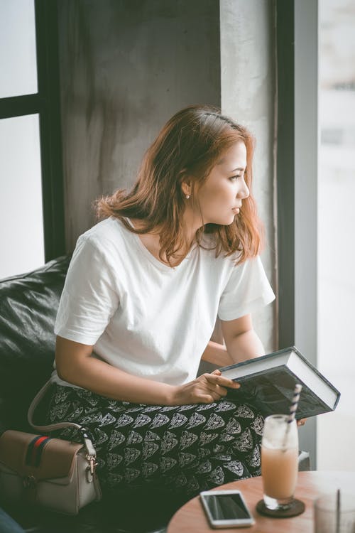 女人坐在沙发上的椅子上拿着本书 · 免费素材图片