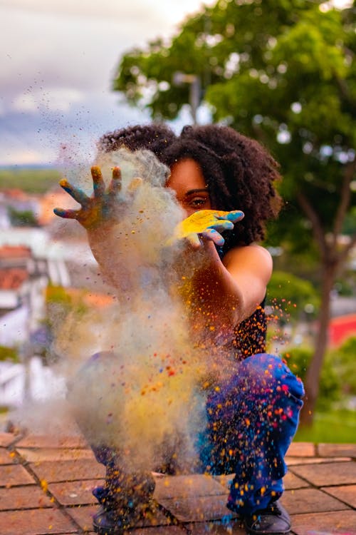 不可识别的黑人妇女在路堤上洒红节期间创建多彩的灰尘 · 免费素材图片