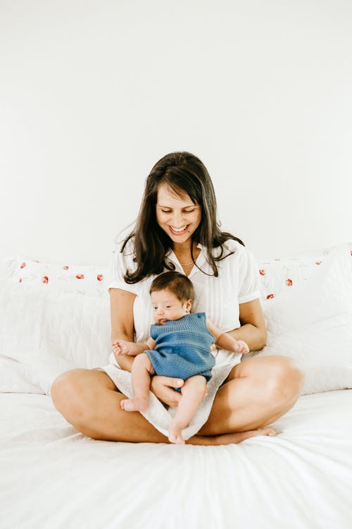 坐在床上抱着婴儿的微笑妇女的照片 · 免费素材图片