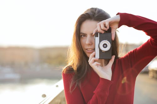 女人在红色的长袖毛衣，用相机拍照的选择性焦点肖像照片 · 免费素材图片
