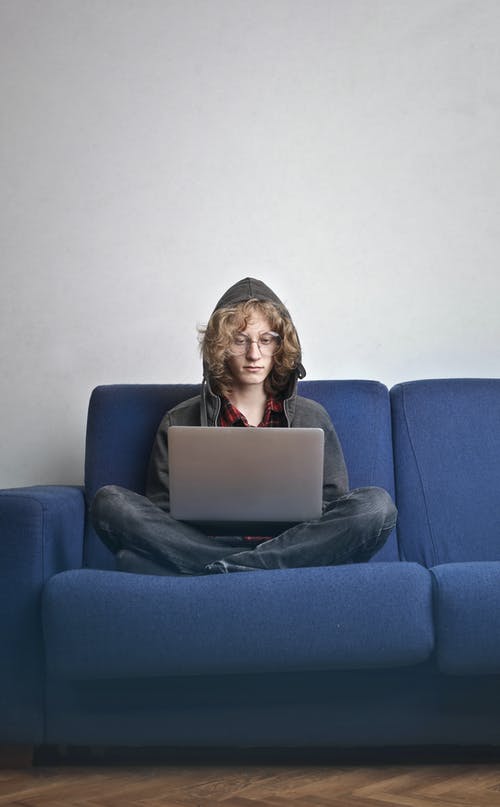 坐在蓝色的沙发上，用一台笔记本电脑的人的照片 · 免费素材图片