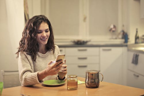 年轻女子喝茶和使用智能手机 · 免费素材图片