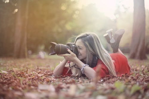 微笑在森林里的专业照片相机上拍照的女人 · 免费素材图片