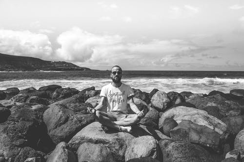 坐在海边岩石上的人的灰度照片 · 免费素材图片