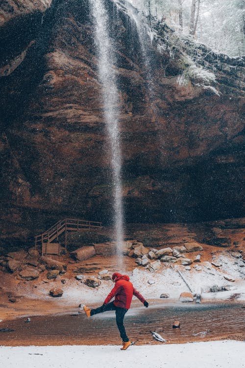 站在瀑布附近的红色连帽衫的男人 · 免费素材图片
