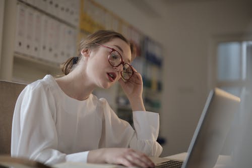 白色的长袖衬衫，戴着眼镜使用便携式计算机的女人 · 免费素材图片