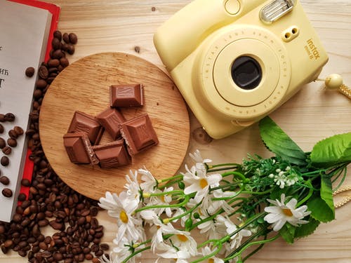 即时照片相机靠近室内的巧克力和洒了的咖啡豆 · 免费素材图片