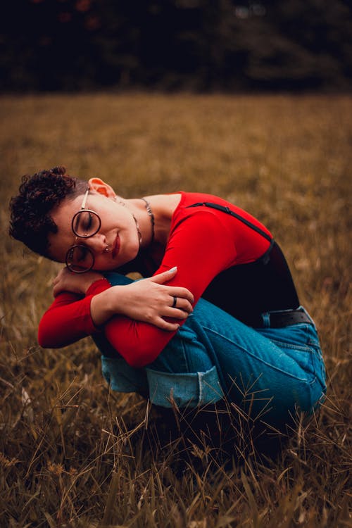 红顶和蓝色牛仔牛仔裤，坐在草地上的女人 · 免费素材图片