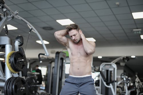 在健身房锻炼期间，裸露躯干的肌肉型男用手加热颈部肌肉 · 免费素材图片