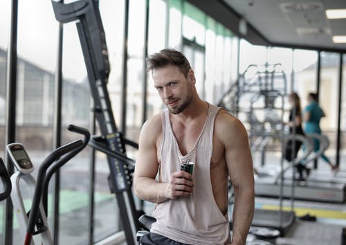 年轻肌肉男运动员锻炼后休息，在现代健身房喝能量饮料 · 免费素材图片