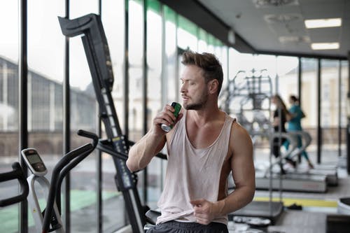 在现代健身房锻炼休息期间坚强的年轻运动员喝能量饮料 · 免费素材图片