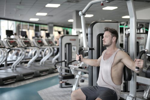 白色背心和灰色短裤坐在健身器材上的男人 · 免费素材图片