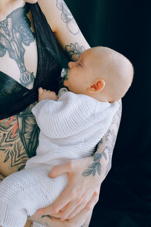 在演播室播种纹身的母亲抱着安抚奶嘴的婴儿在睡觉 · 免费素材图片