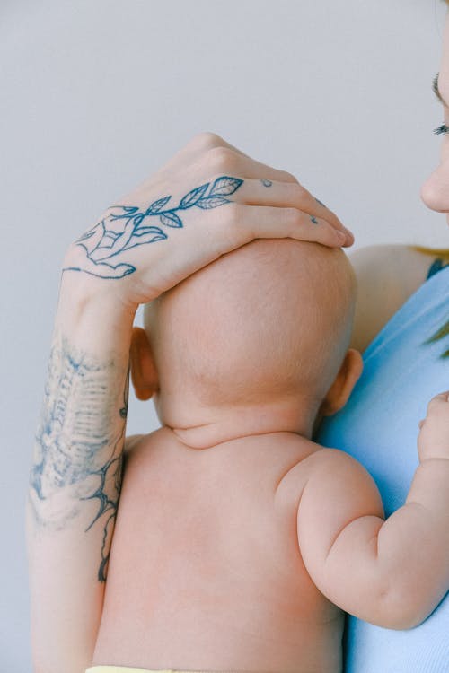 在房间里抱着蹒跚学步的同时tattoo着新生儿纹身头的裁剪母亲 · 免费素材图片