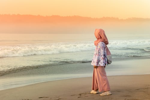 橙色头巾站在日落期间在海滩上的女人 · 免费素材图片