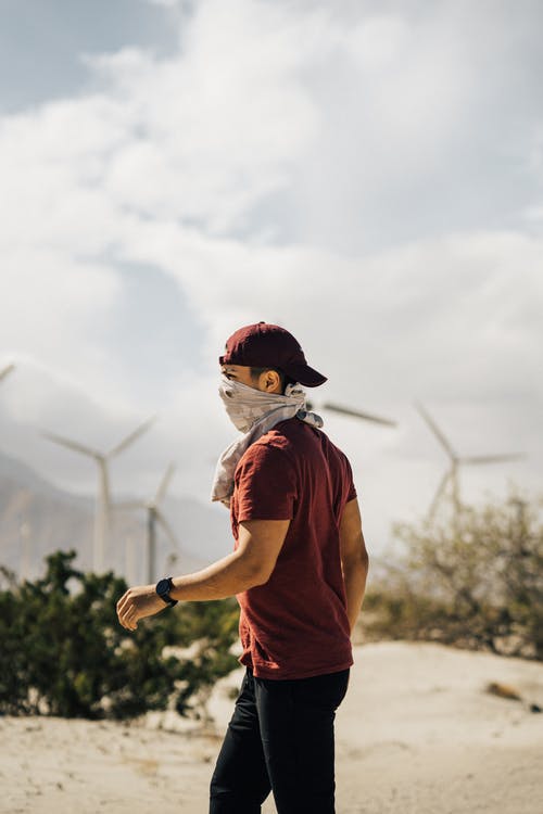 围巾在风车附近的沙质地形地形行走的脸上变得面目全非的人 · 免费素材图片