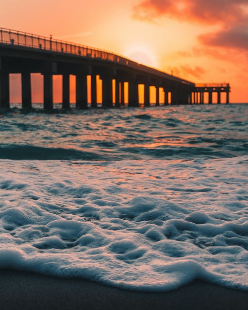 泡沫波的海洋和码头对橙色落日的天空 · 免费素材图片