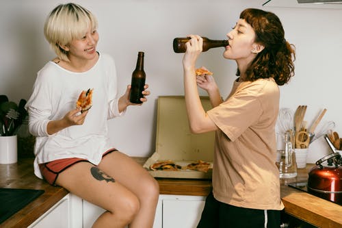 女朋友在家里的厨房里吃披萨和喝啤酒 · 免费素材图片