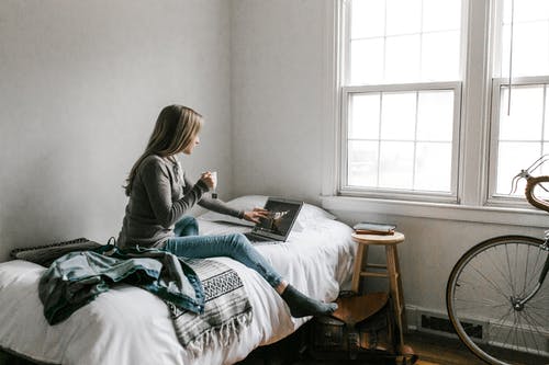 坐在床上看书的灰色长袖衬衫的女人 · 免费素材图片