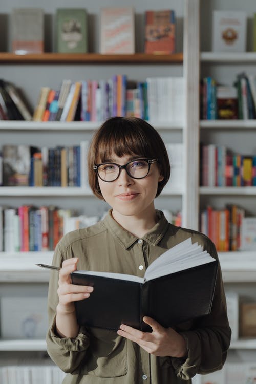 女人穿着绿色按钮衬衫穿着黑色镜框的眼镜看书 · 免费素材图片