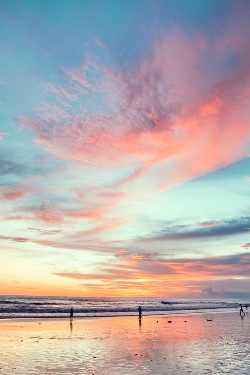 沙滩上的匿名游客在日落时明亮的天空下 · 免费素材图片
