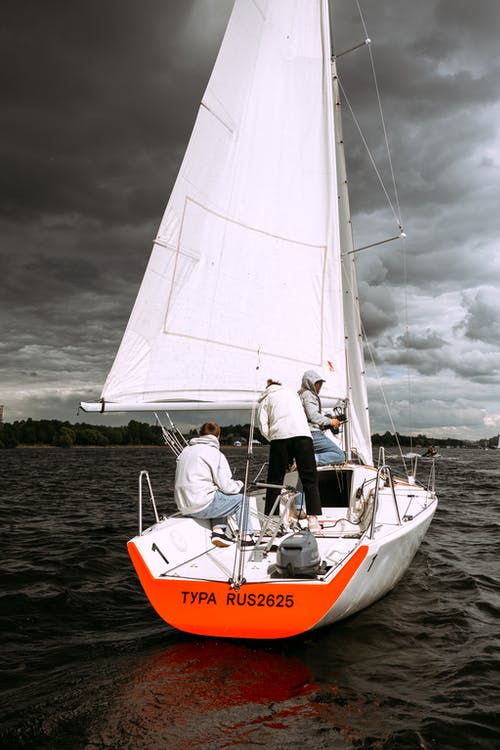 期间在海上的橙色和白色帆船上骑白衬衫和黑色裤子的人 · 免费素材图片