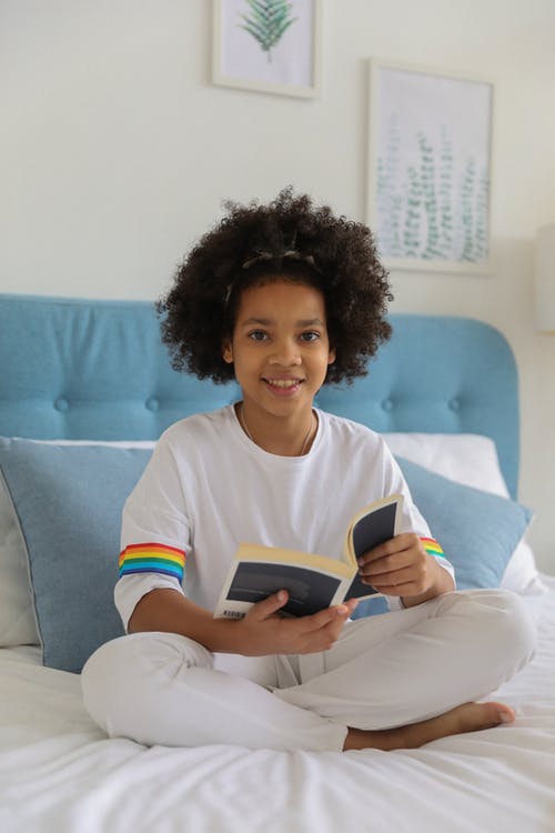 有书的快乐的微笑的黑人女孩在床上 · 免费素材图片