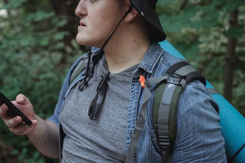 作物与智能手机在树林里的男性徒步旅行者 · 免费素材图片