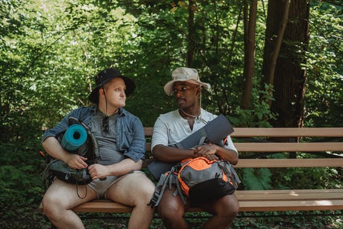 在森林里的长椅上休息的多样背包客 · 免费素材图片