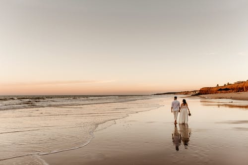 夫妇在婚礼上穿沿着海边散步 · 免费素材图片
