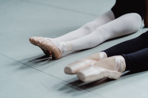 不可识别的教练和小芭蕾舞女演员在工作室里指出脚伸展 · 免费素材图片