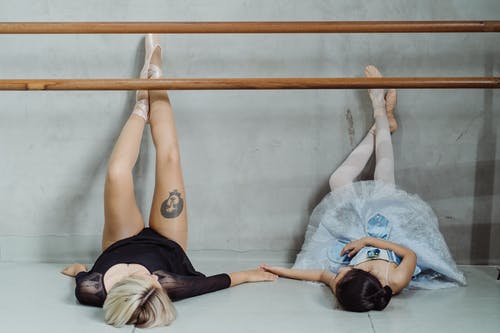 芭蕾舞教练与躺在地板上的小芭蕾舞演员牵手 · 免费素材图片