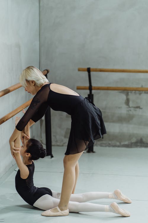 年轻的女教练，帮助小民族芭蕾舞演员在训练过程中向后伸展 · 免费素材图片