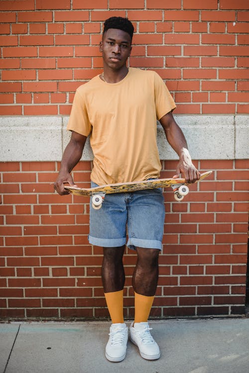 冷静与滑板站在砖墙附近的黑人男子 · 免费素材图片