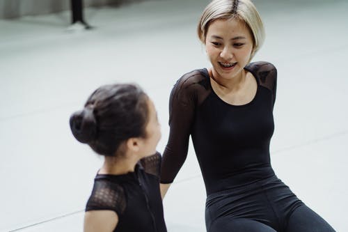 性格开朗的亚洲女芭蕾舞教练和学员坐在地板上 · 免费素材图片