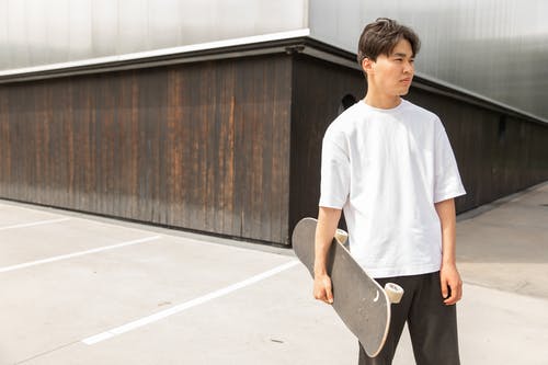 时尚年轻的亚洲男性，与滑板在手在当代建筑附近的街道上冷 · 免费素材图片