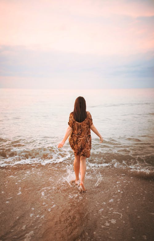 在朝着海浪的海滩上行走的匿名女子 · 免费素材图片
