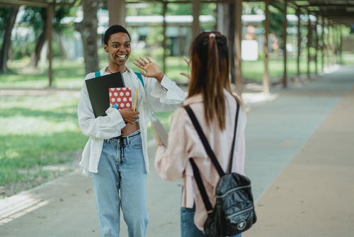 快乐的黑人女学生在人行道上问候匿名最好的朋友 · 免费素材图片