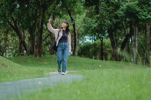 微笑的年轻亚裔妇女谈话通过智能手机，当走在公园时 · 免费素材图片