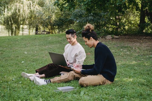 高兴的男学生与笔记本电脑在公园里做作业 · 免费素材图片