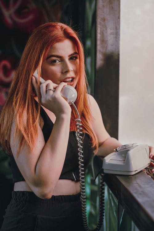 时尚年轻的红发女郎女士通过老式旋转电话交谈 · 免费素材图片