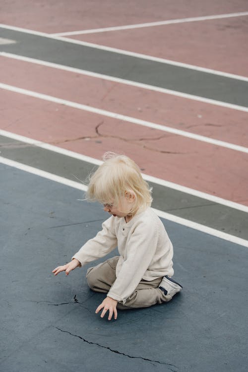 米色毛衣和灰色的裤子，坐在灰色的水泥地板上的女孩 · 免费素材图片