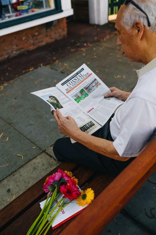 白衬衫和黑裤子坐在棕色的木凳上看报纸的人 · 免费素材图片