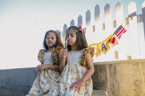 2个女孩穿着白色和棕色的花裙子，吹泡泡 · 免费素材图片