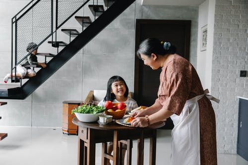 坐在桌上的快乐的矮小的亚裔女孩，当祖母服务午餐与新鲜的菜时 · 免费素材图片