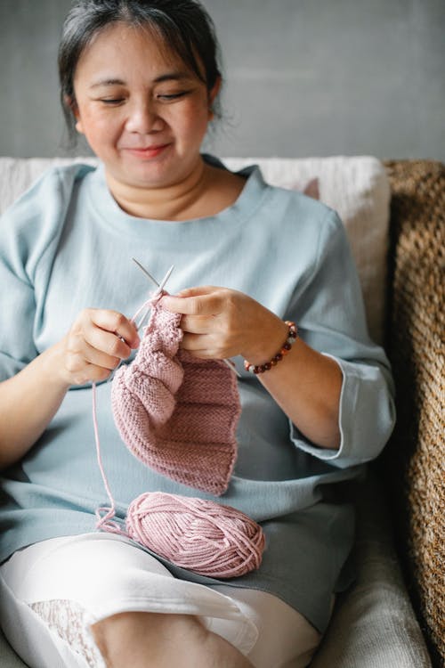 作物亚洲女人在沙发上编织服装 · 免费素材图片